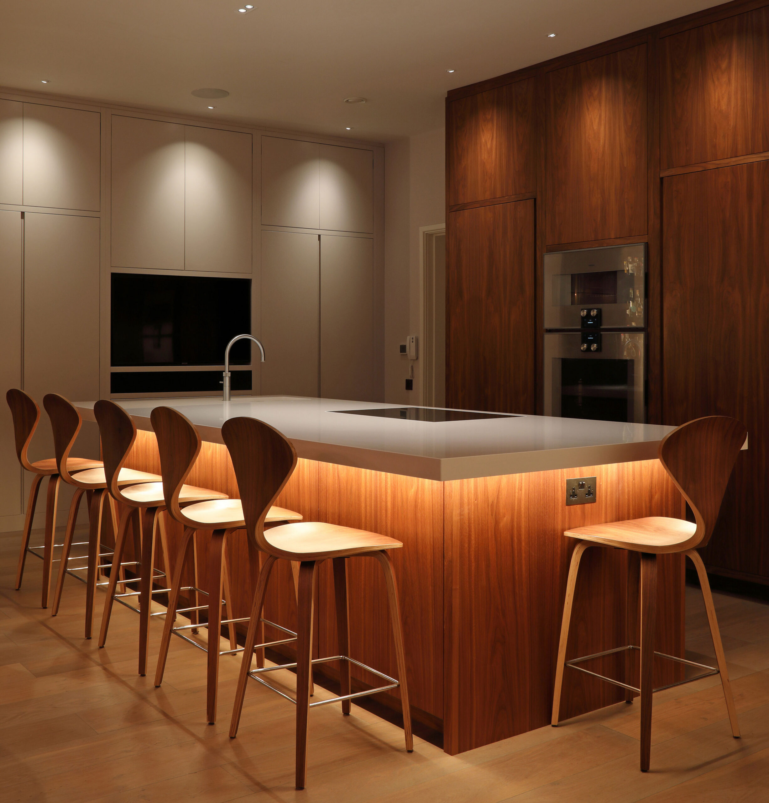 Cocina moderna con isla central en madera, cubierta clara y barra con iluminación indirecta